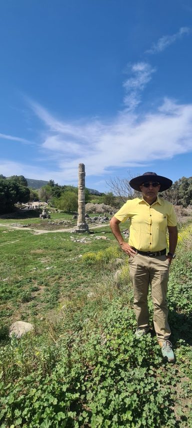 The Temple of Artemis at Ephesus Person in a yellow shirt and hat stands beside a tall stone column in a green landscape.
